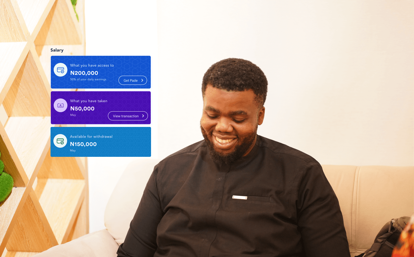 A smiling man in a black shirt sits on a beige couch. To his left, digital UI boxes display salary information, including accessible funds, amount taken, and withdrawal options in Nigerian Naira.